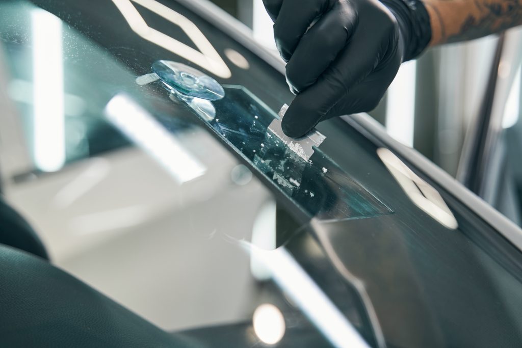 Close-up of a technician wearing black gloves using a tool to repair rock chips on a car windshield. 